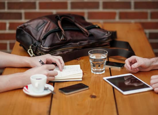 Cups of coffee on a table. Two sets of hands near them on either side of the table.